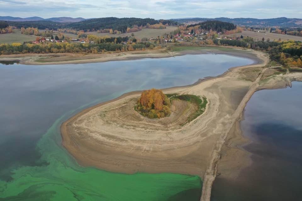 Ostrůvek na Lipně a obnažené dno u břehu, v pozadí vesnice