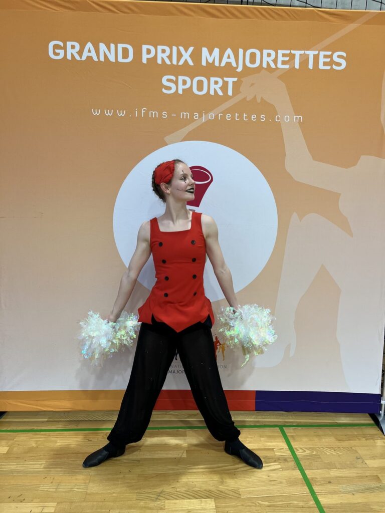 Sólistka s pompony před stěnou Grand Prix Majorettes Sport
